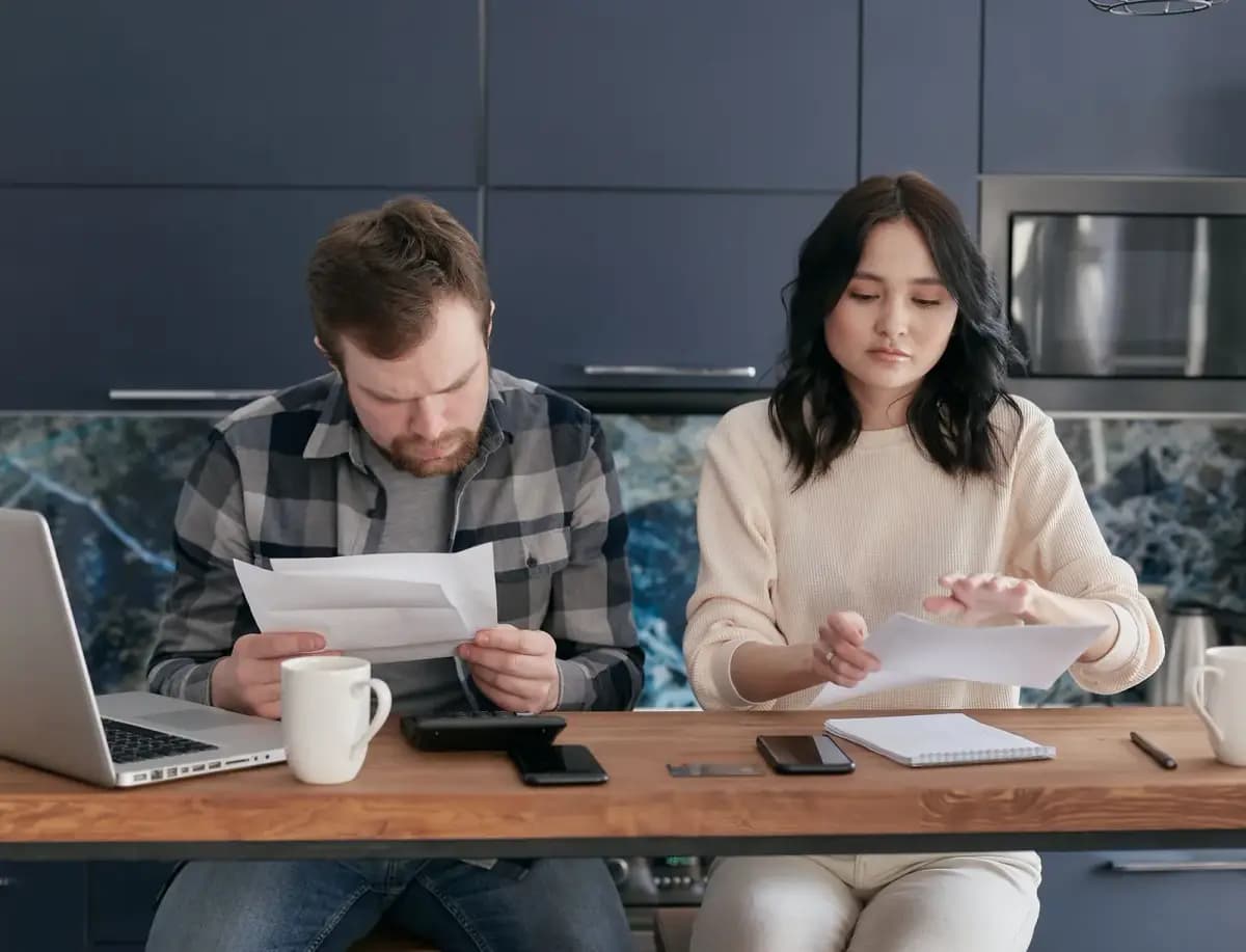 Casal na mesa conferindo documentos, notebook e café