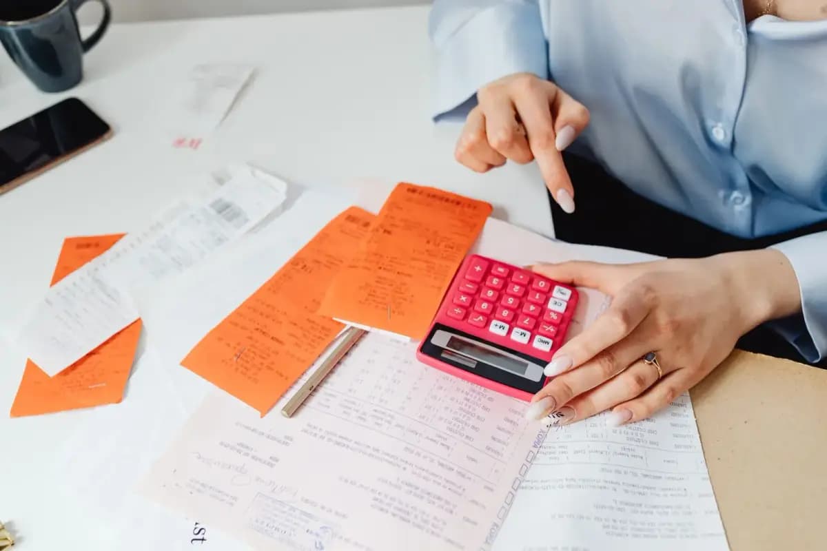 Mãos com calculadora rosa e notas fiscais sobre a mesa