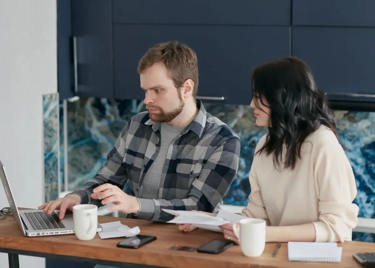 Casal na mesa com notebook e café organizando as finanças