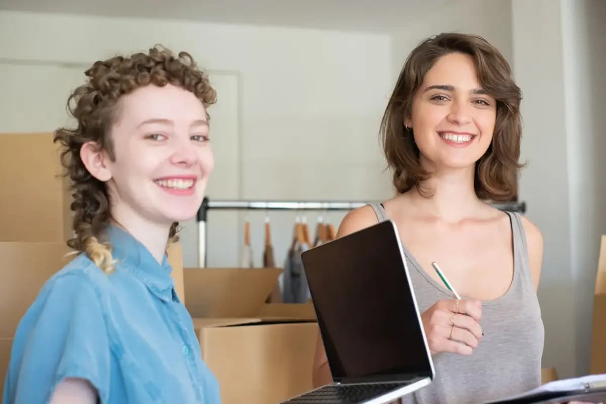 Duas sócias com notebook entre caixas e arara de roupas
