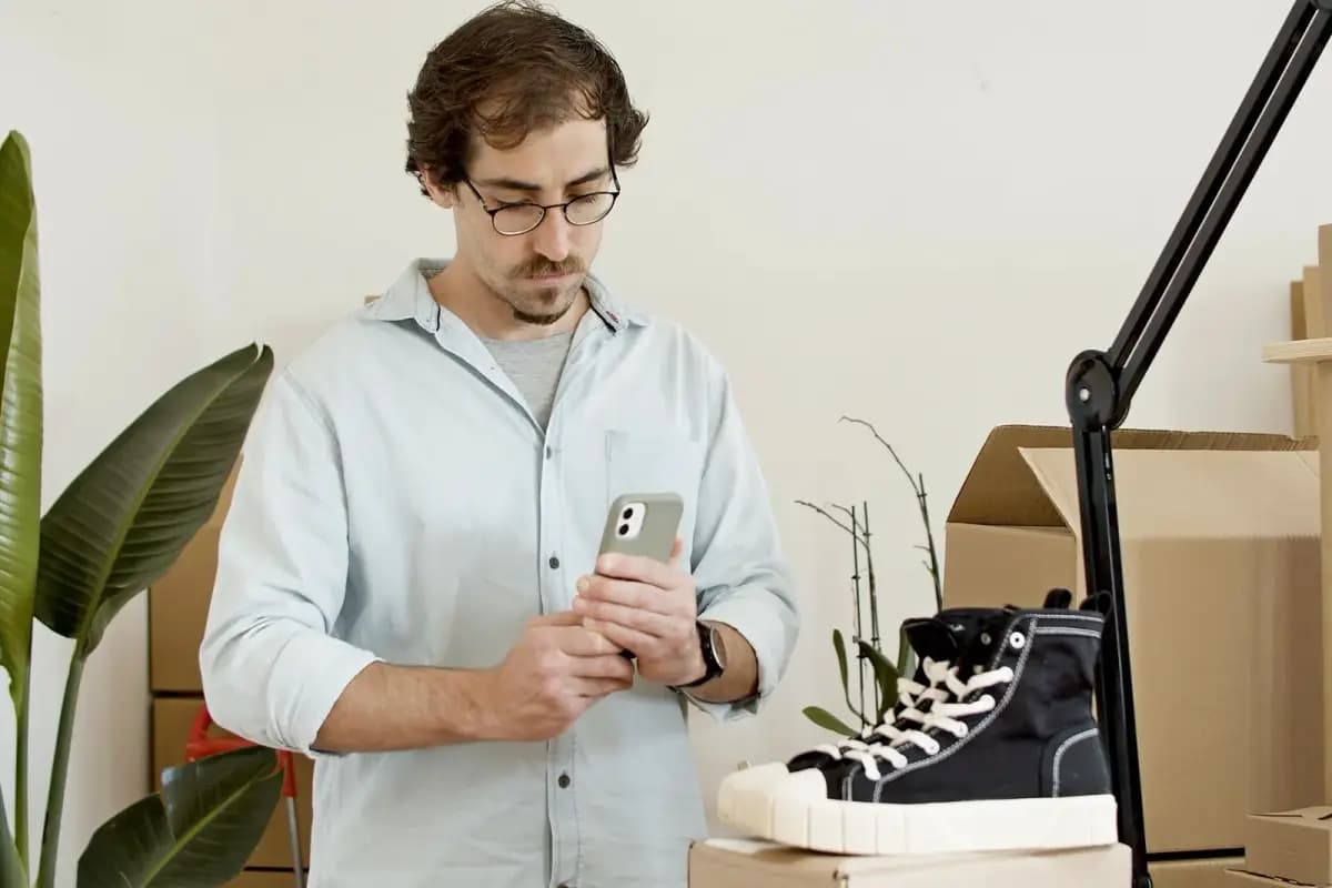 Homem fotografando um tênis com o celular em ateliê com caixas